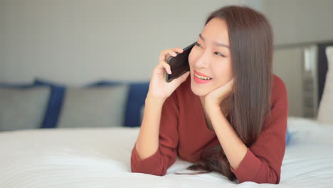 Portrait-of-Young-Asian-Woman-Making-Phone-Call-With-Smartphone,-Lying-on-Bed,-Close-Up