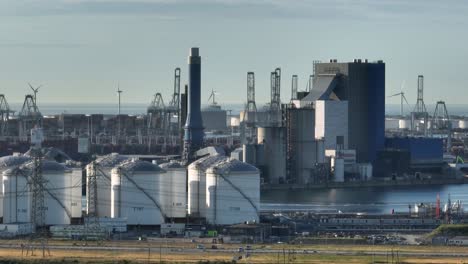 Luftaufnahme-Des-Turms-Eines-Kohlekraftwerks-Mit-Öllagertanks-Und-Rotierenden-Windturbinen-An-Sonnigen-Tagen---Hafen-Von-Rotterdam,-Niederlande