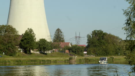 Motorboat-on-a-river-sail-past-the-cooling-tower-of-a-coal-fired-power-plant