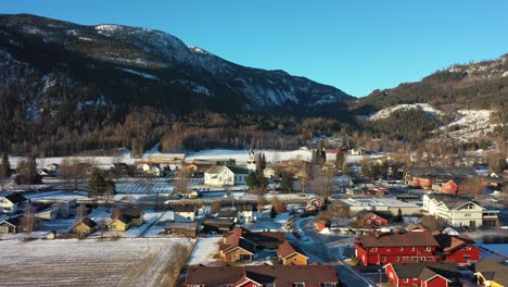 Approaching-Nesbyen-church-in-Hallingdal-Norway-during-beautiful-morning-sunlight---Golden-hour-aerial-with-winter-landscape-surroundings