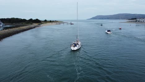 Aerial-view-following-behind-luxury-sailboat-travelling-along-scenic-river-estuary