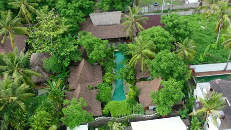 aerial-top-down-of-turquoise-pool-and-joglo-villas-surrounded-by-coconut-trees-on-tropical-island-in-Gili-Trawangan
