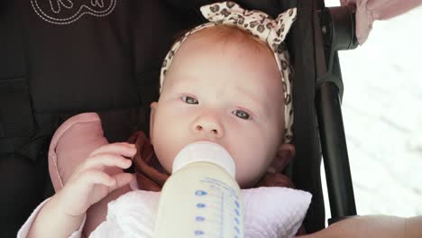 Little-baby-girl-drinking-her-milk-in-a-baby-stroller