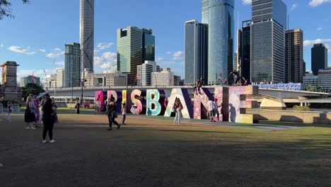 Wide-shot-of-happy-children-and-adults-having-fun-climbing-up-artistic-block-letter-of-Brisbane-city-and-taking-photos-of-iconic-landmark-with-downtown-cityscape-as-backdrop,-Queensland,-Australia