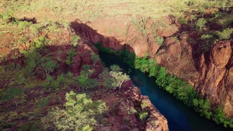 Drone-footage-flying-left-to-right-revealing-a-deep-red-gorge-with-a-calm-river-flowing-through-it
