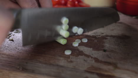Slow-pan-left-to-right-of-spring-onions-being-chopped-on-wooden-chopping-board