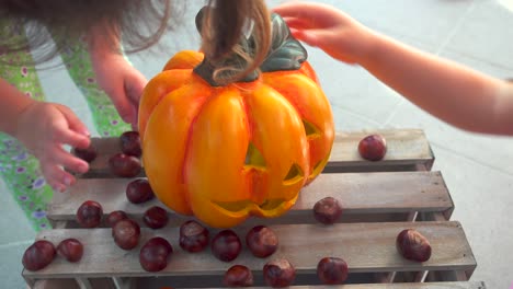 Little-girl-playing-feeding-chestnuts-to-halloween-pumpkin,-child-play,-holiday-decoration,-unrecognizable