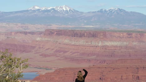 Slow-motion-shot-of-female-tourist-showing-hand-peace-sign-in-front-of-view-from-Dead-Horse-Point-State-Park-in-Utah,-USA
