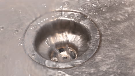 Close-up-slow-motion-shot-of-water-draining-down-a-stainless-steel-sink