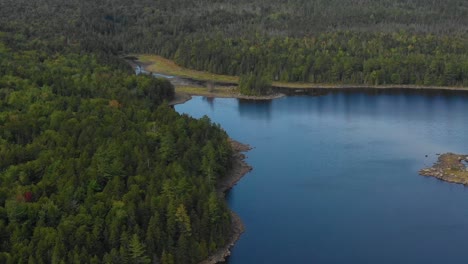 Aerial-footage-of-a-remote-lake-in-northern-Maine-zooming-in-towards-lake-inlet-with-forest-and-mountains-in-background