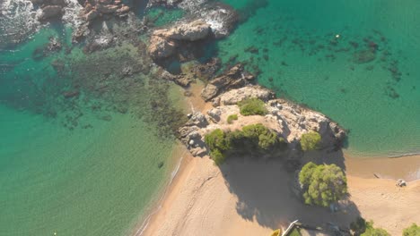 Aerial,-top-down,-birdseye,-drone-shot,-sideways,-over-rocky-coast,-turquoise-sea-and-the-Lloret-de-Mar-beach-,-in-Santa-Cristina,-Cala-Boadella,-Costa-Brava,-in-Catalonia,-Spain