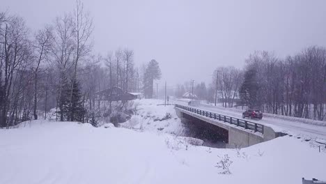 SLOW-MOTION-Aerial-shot-of-an-SUV-following-a-truck-with-a-snowmobile-trailer-over-a-bridge-in-a-snow-storm