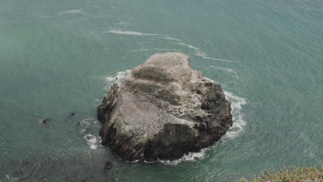 Weitwinkelaufnahme-In-Zeitlupe-Aus-Hohem-Winkel-Von-Wellen,-Die-Gegen-Einen-Riesigen-Felsen-Im-Pazifik-Krachen