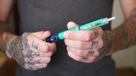A-young-man-with-tattoos-takes-of-the-protection-from-an-insulin-pen,-adjust-the-dosage-and-prepares-for-injection