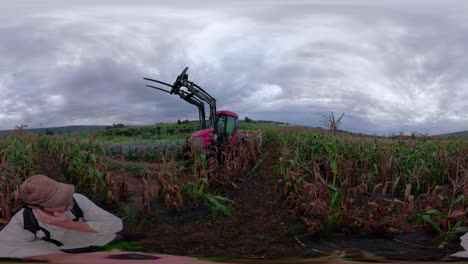 360-vr-of-man-with-selfie-stick-moving-through-corn-field-while-tractor-moves-through-it