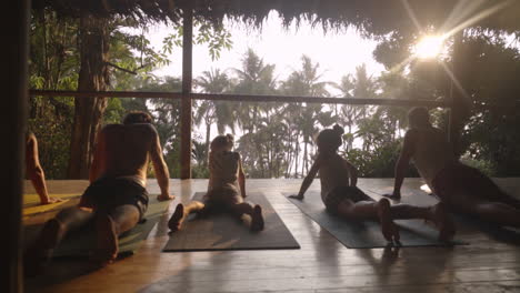 Slide-right-along-a-family-of-travelers-enjoying-a-sunset-meditation-and-yoga-session-on-a-wooden-porch-overlooking-the-rainforest-and-jungle-leading-out-to-the-beach