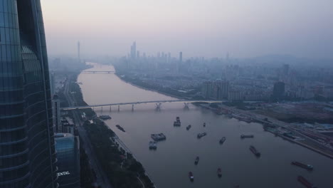 Aerial-shot-of-Pazhou-area-of-Guangzhou-with-office-building,-pearl-river,-and-boats-anchored-and-city-downtown-in-the-distance