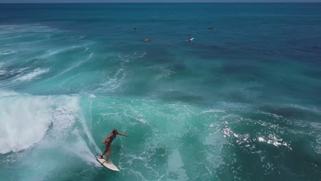 Luftaufnahme-Einer-Surferin-Im-Bikini,-Die-Während-Einer-Surfsession-Im-Blauen-Meer-Von-Costa-Rica-Eine-Schnelle-Welle-Auf-Ihrem-Surfbrett-Fängt-Und-An-Die-Küste-Reitet
