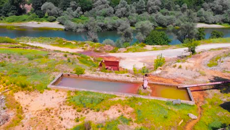 Aerial-of-a-girl-in-a-long-dress-standing-on-concrete-water-reservoir-near-abandoned-mine-and-Arda-river
