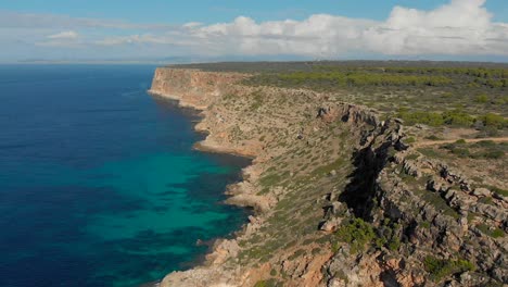 Drone-footage-flying-over-the-ocean-towards-the-cliffs-with-blue-and-turquoise-water-underneath