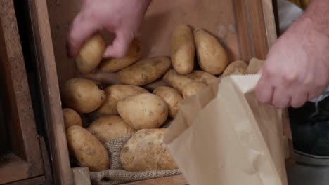 Close-up-of-picking-potatoes-from-a-rustic-wooden-box-and-placing-them-in-a-paper-bag