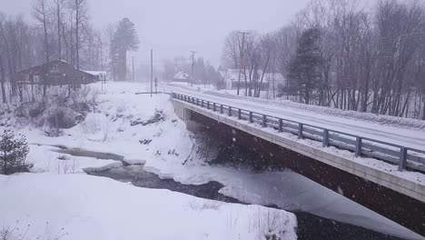SLOW-MOTION-Aerial-shot-approaching-closer-to-a-bridge-crossing-an-icy-river-during-a-snow-storm