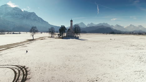 Aerial-clip-of-a-Church-in-the-middle-of-big-fields,-with-mountains-in-the-background,-during-winter