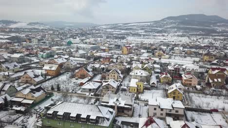 Flying-over-suburbs-of-city-with-colorful-houses-and-snow-covered-roofs,-Bistrita,-Romania