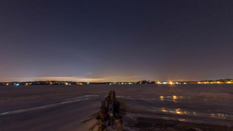 Timelapse-of-the-stars-rotating-across-the-night-sky-above-a-frozen-river-in-front-of-a-wooden-jetty-on-a-very-cold-night