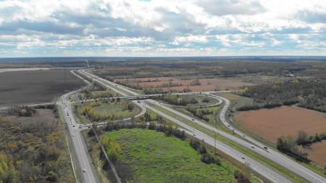 Aerial-footage-just-outside-of-Ottawa,-Ontario-of-vehicles-on-a-busy-highway-with-over-and-underpasses-and-hydro-lines-crossing-over-with-autumn-forests-surrounding-everything-and-fields
