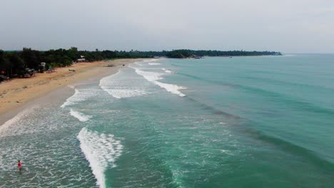 Aerial,-static,-drone-shot-of-people-on-the-beach,-while-waves-hits-a-paradise-coast,-near-Trincomalee-city,-on-a-cloudy-day,-in-Gokanna,-in-the-Eastern-Province,-of-Sri-Lanka