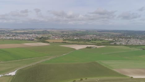 Aerial-tracking-north-from-Maiden-Castle,-the-towns-of-Dorchester-and-Poundbury-is-visible-in-the-background