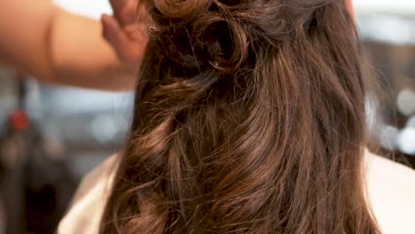 A-professional-stylist-puts-the-finishing-touches-on-a-brunette-woman's-hairdo-with-long-brown-curls,-PAN-UP