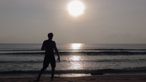 Man-walking-towards-ocean-by-sunrise-in-Asia-to-take-morning-swim-in-slow-motion