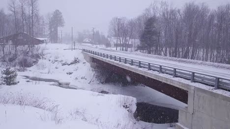 SLOW-MOTION-Aerial-shot-approaching-a-bridge-corssing-over-an-icy-river-during-a-snow-storm