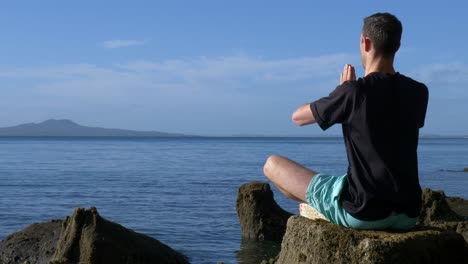 Junger-Fitter-Mann,-Der-Morgens-In-Yoga-pose-Auf-Felsen-Am-Strand-Meditiert