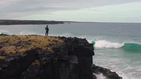 Man-watches-the-waves-rolling-in-and-out-from-a-cliff-in-slow-motion