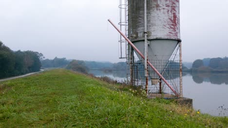 Drone-shot-of-an-old-metal-silo-overlooking-a-reflective-lake-on-an-autumn-morning