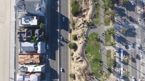 Birds-eye-view-of-traffic-driving-in-city-beach,-shot-on-drone-panning-sideways-looking-directly-down