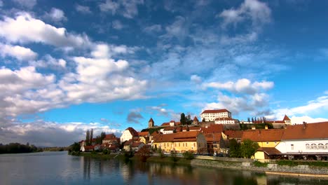 Old-town-of-Ptuj,-Slovenia,-view-from-footbridge-across-Drava-river-on-old-town-and-castle-dominating-the-cityscape
