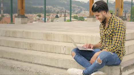 Handsome-man-siting-on-stairs-using-laptop-outdoors