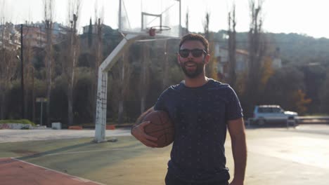 Male-basketball-player-stands-with-ball-under-arm-after-training-handheld-video-portrait