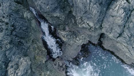 Aerial-tracking-top-down-over-a-rocky-fissure-on-the-coast-during-rough-sea-tides