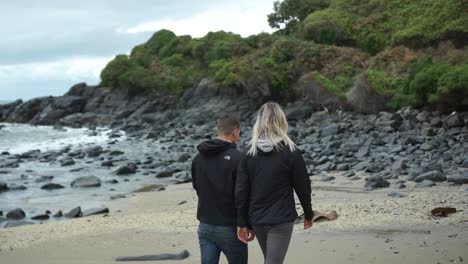 Young-attractive-couple-walking-on-beach-in-Bluff,-New-Zealand-on-cloudy-day