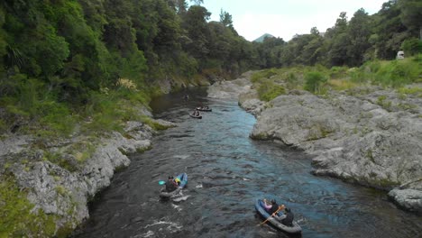 SLOWMO---Kayaking-tour-paddle-boats-through-canyon-on-Pelorus-river,-New-Zealand-with-native-forrest-and-rock-boulders---Aerial-Drone