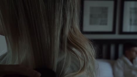SLOWMO---Young-beautiful-blond-woman-brushing-hair-and-man-lying-on-bed-in-luxury-boutique-hotel-room