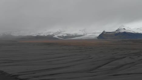 Aerial-panning-shot-of-mountains-behind-a-black-sand-beach-in-Iceland
