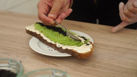 Preparing-Avocado-on-toast-bread-with-black-and-white-sesame-seeds-and-hummus