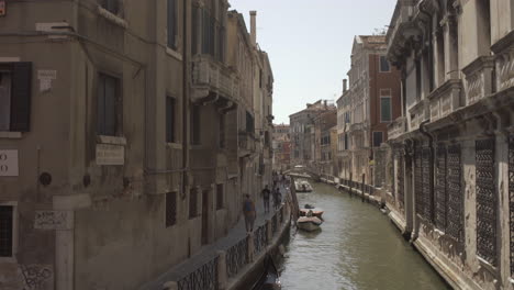 Tilt-down-on-Tourists-walking-in-Historic-Wide-canal-in-Venice-at-a-sunny-day,-Italy