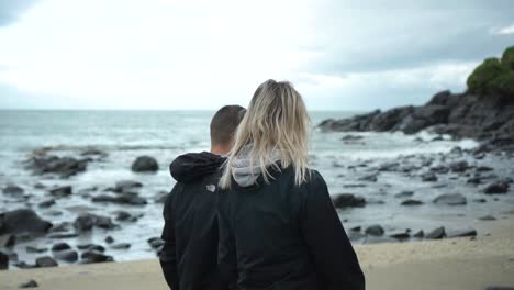 SLOWMO---Young-attractive-couple-walking-on-beach-in-Bluff,-New-Zealand-on-cloudy-day